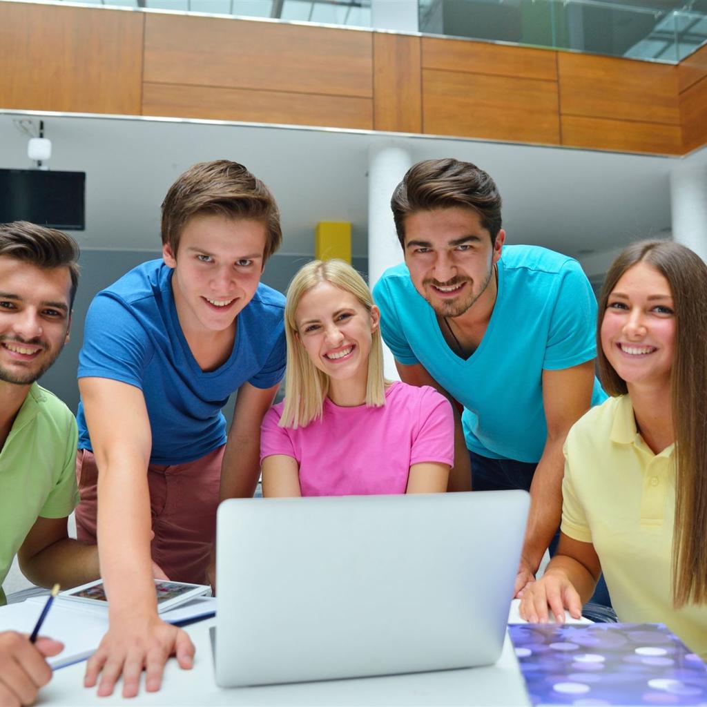 Eine Gruppe von 5 Studierenden sitzen vor einem Laptop und lächeln freundlich in die Kamera