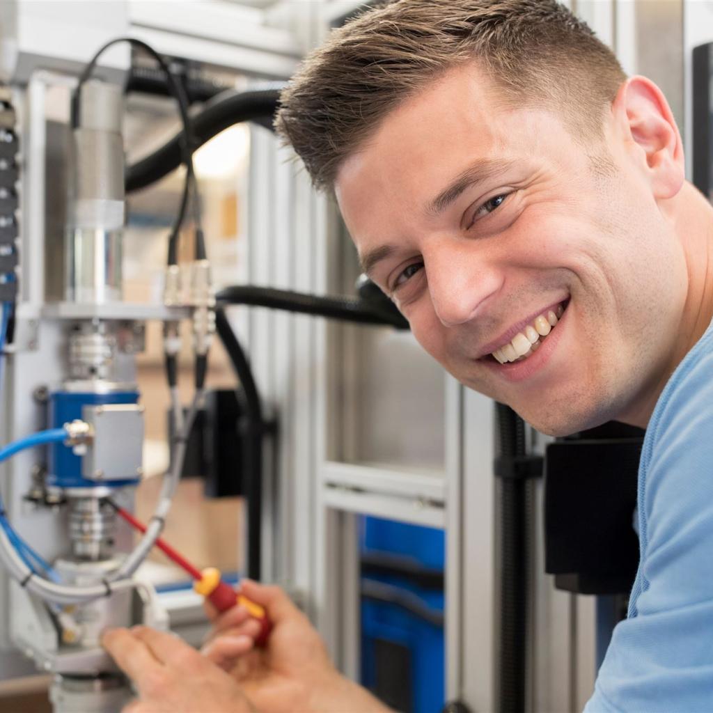 Ein junger Mechaniker vor einer technischen Gerätschaft lächelt in die Kamera