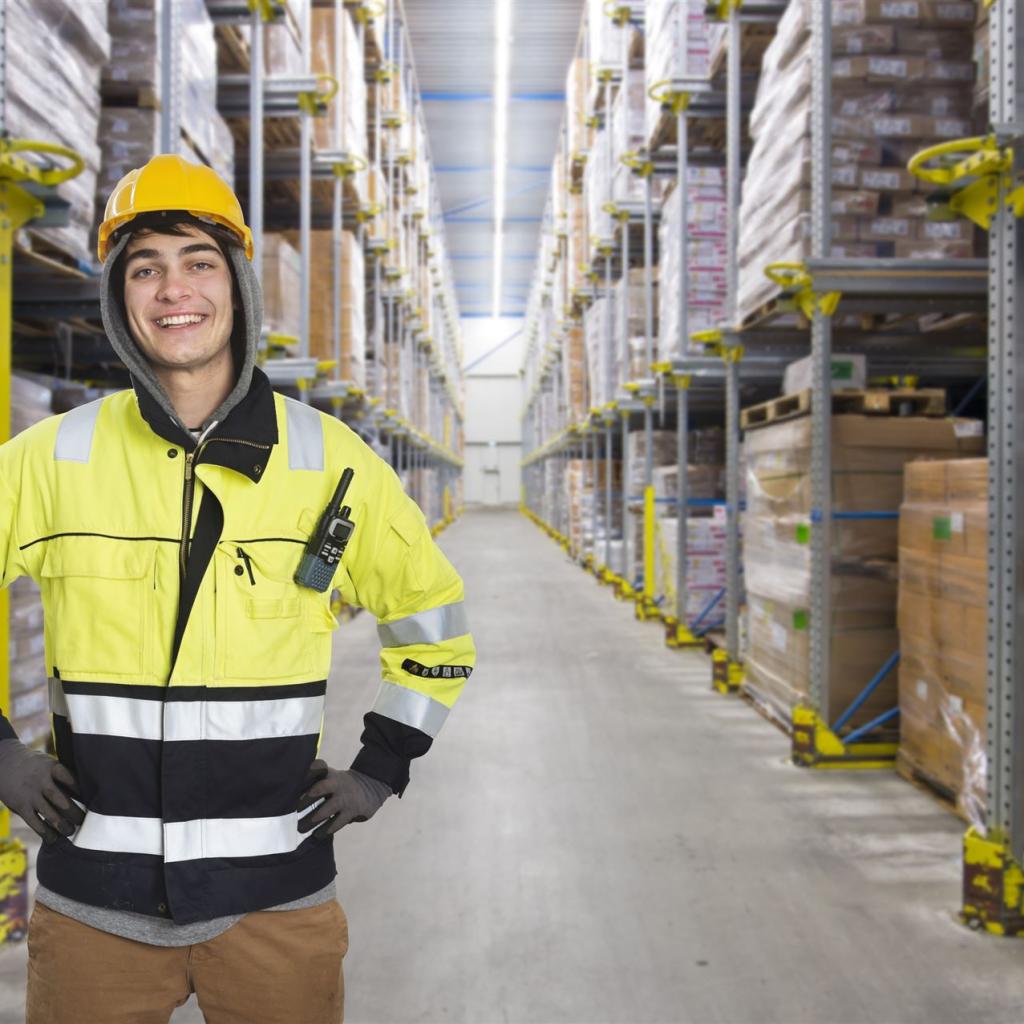 Ein junger Fachlagerist mit gelber Warnkleidung inmitten ein Hochregallagers