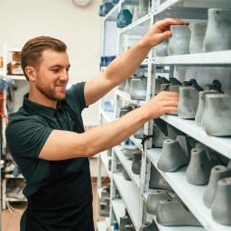 Ein junger Orthopädie Schuhmacher sortiert Schuhleisten in ein Regal