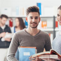 2 Studierende, eine Frau und ein Mann mit Unterrichtsmaterial in den Händen lächeln in die Kamera