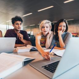 Eine Gruppe junger E-Commerce Kaufleute sitzen vor dem Laptop und diskutieren über ein Konzept