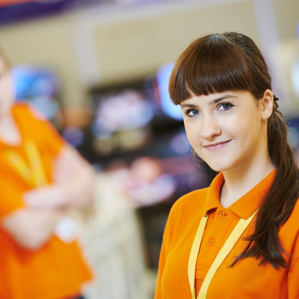 Eine junge Kauffrau im orangefarbenen Firmenshirt in einer Verkaufsabteilung