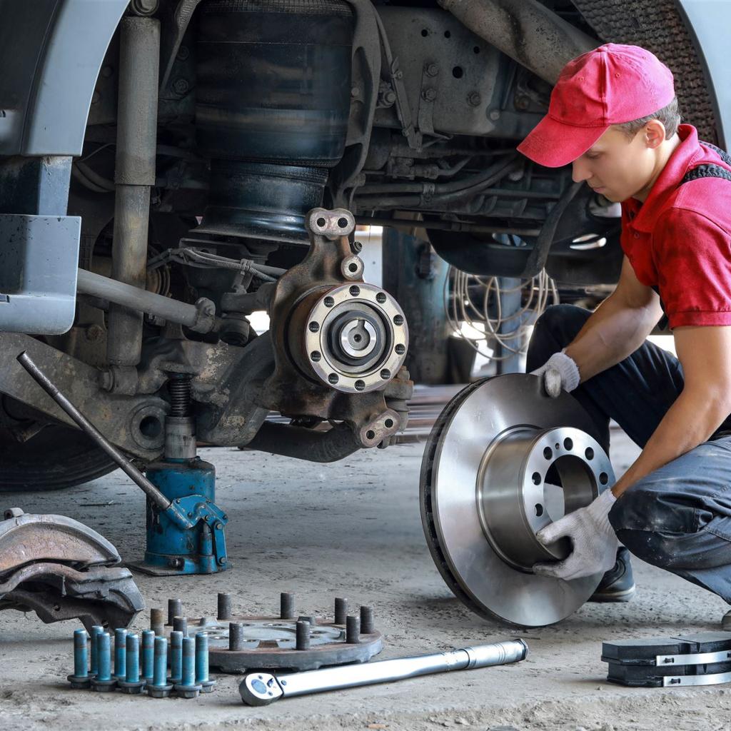 Ein junger Mechatroniker, knieend, wechselt die Bremsscheiben eines Lastkraftwagens
